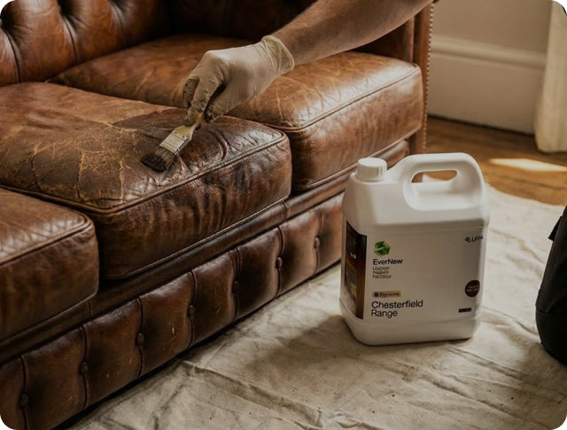 A person wearing a white glove uses a brush to apply a leather restoration product to a brown leather sofa. A large white plastic jug of Everflow Chesterfield Range leather care sits on a drop cloth on the floor nearby.