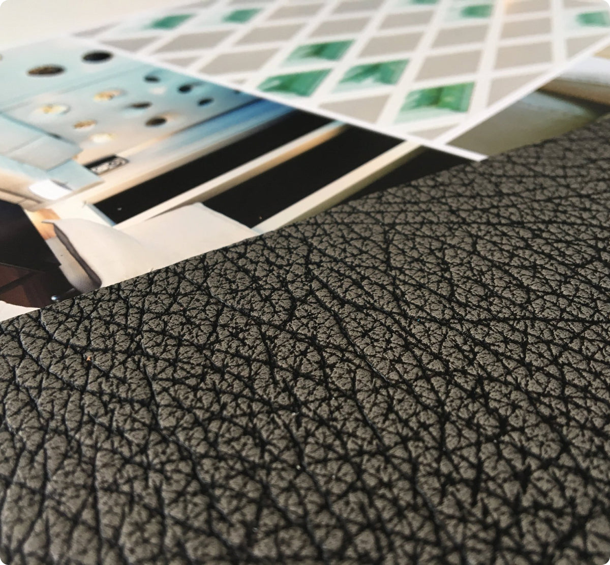 A close-up of a black textured material with a pebbled leather-like surface, with printed sheets partially visible in the background.